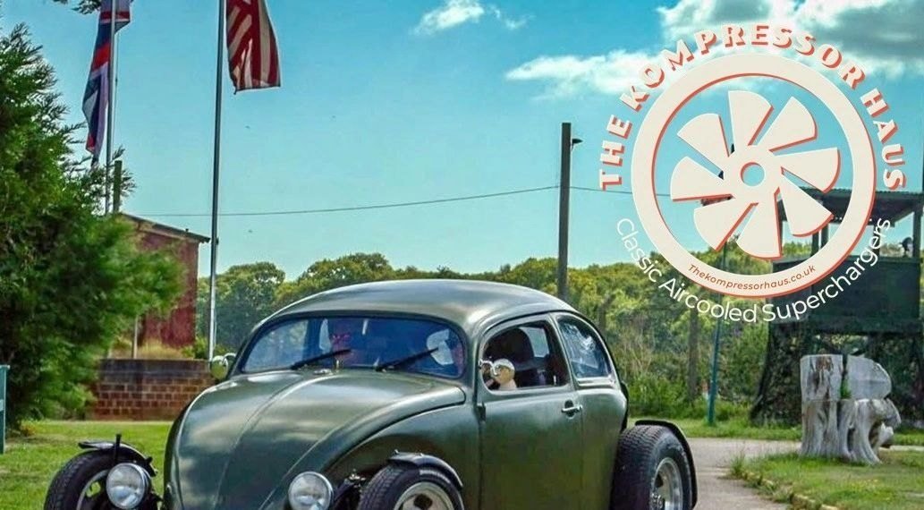 Olive green rat-look Beetle, chopped and slammed, parked on a driveway under
                    flags.