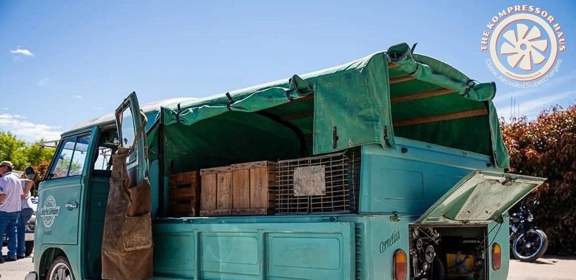 Turquoise Splitscreen single cab pickup at a show with the engine hatch open
                    and wooden crates in the bed.
