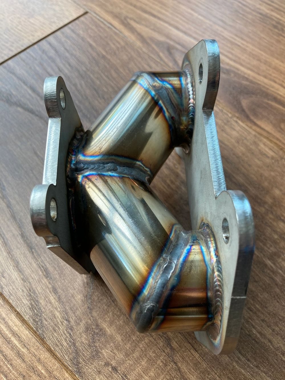 A TIG-welded stainless steel T-tube with laser-cut flanges, the weld beads
                    still showing their heat colours.