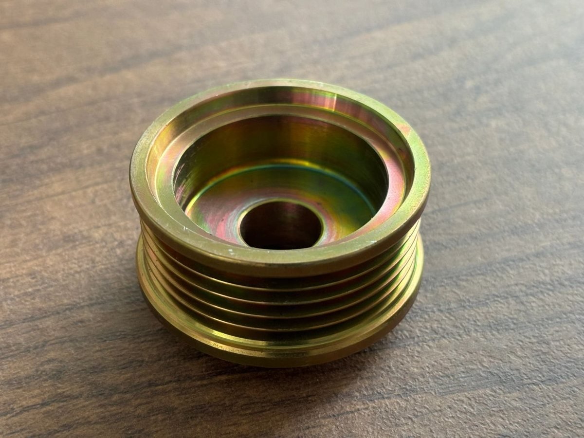 A zinc-plated multi-groove supercharger drive pulley on a workbench.